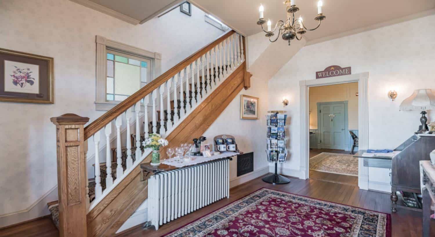 Entry area with light colored wallpaper, hardwood floors, large area rug, and wooden staircase with white spindles leading up to the second floor