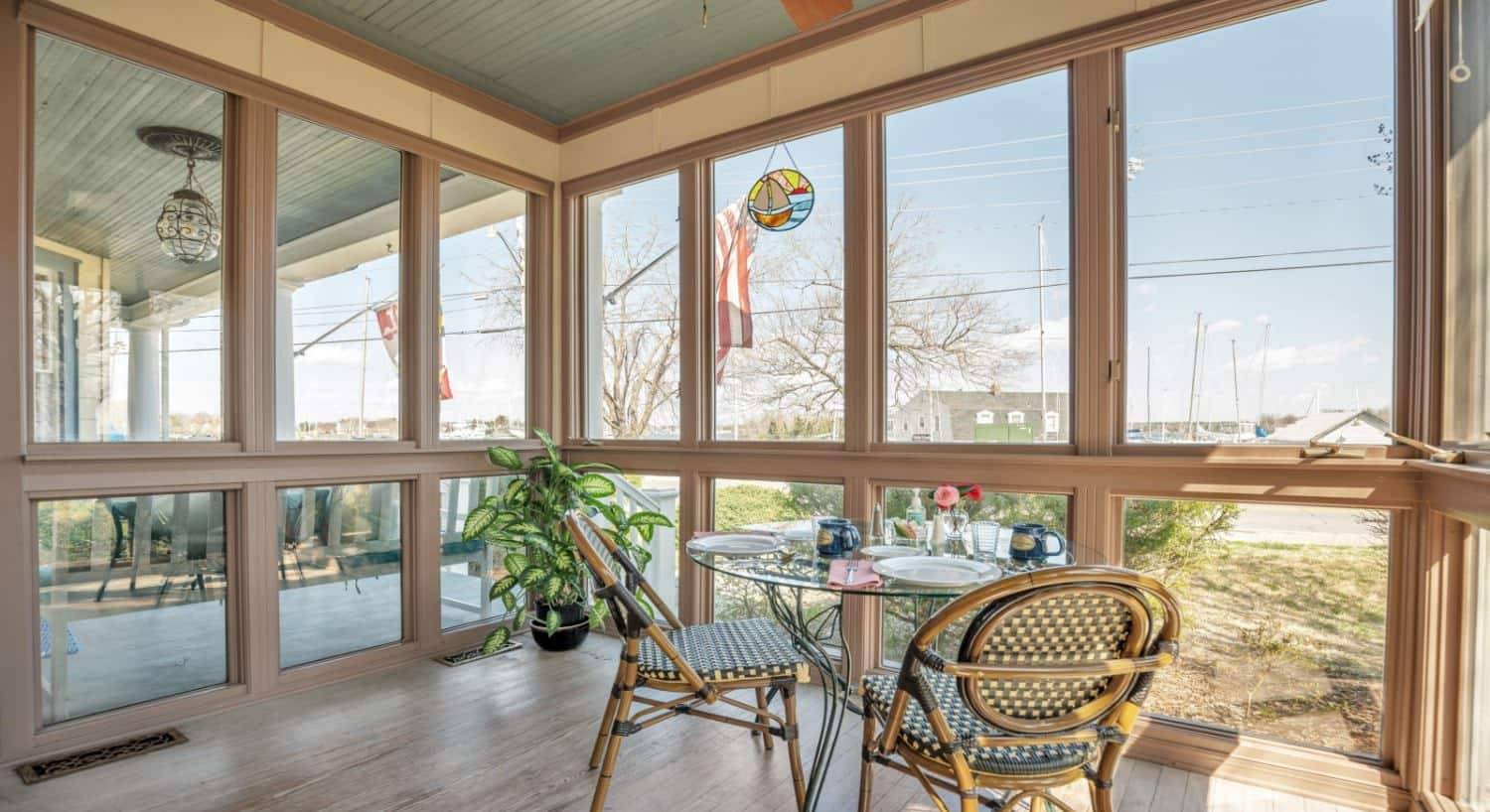 Large enclosed sunroom with glass table and two wicker chairs and a view to the outside