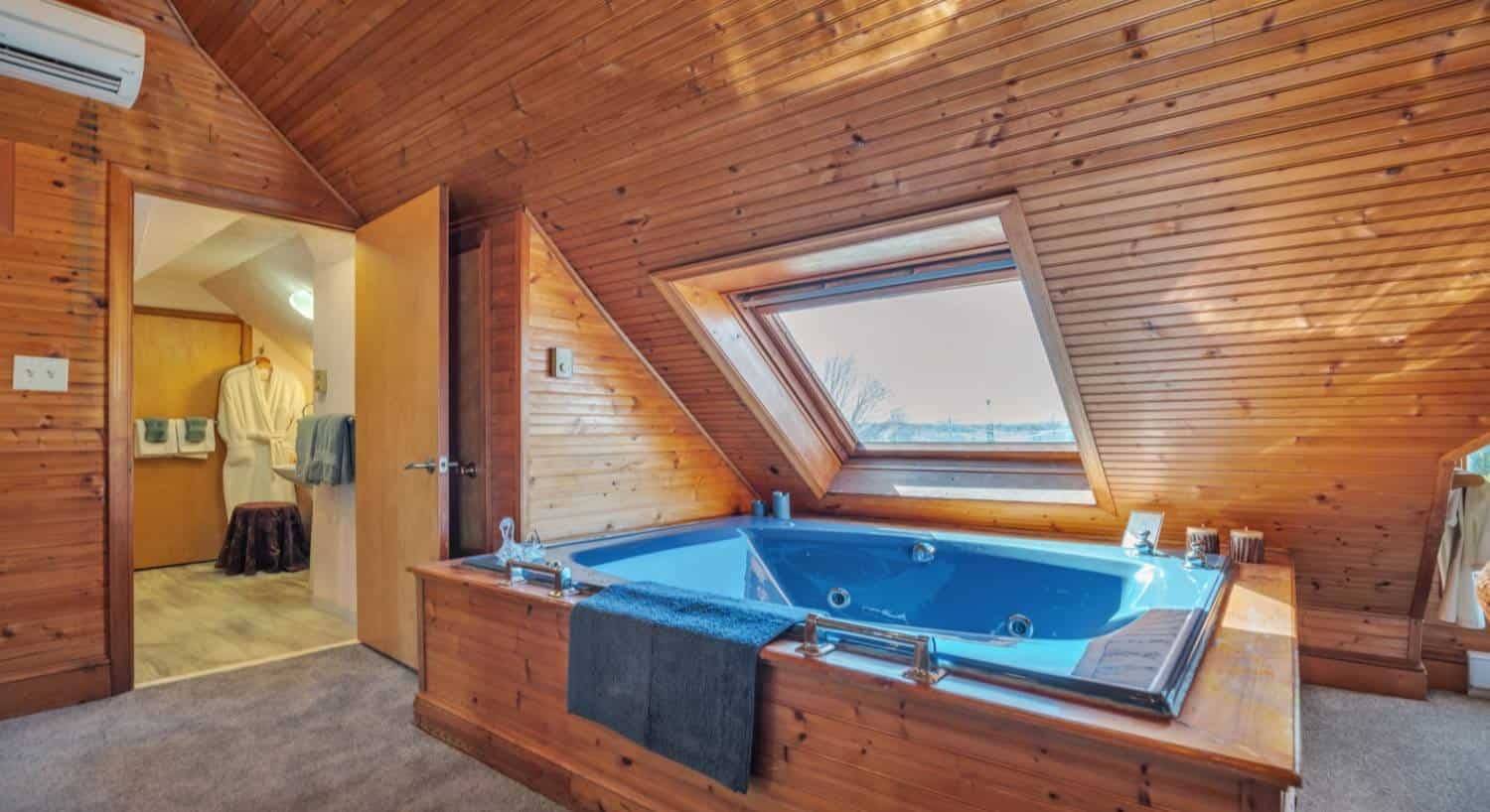 Room with floor to ceiling wood paneling, blue jetted tub surrounded by wood paneling, and large window with views to the outside