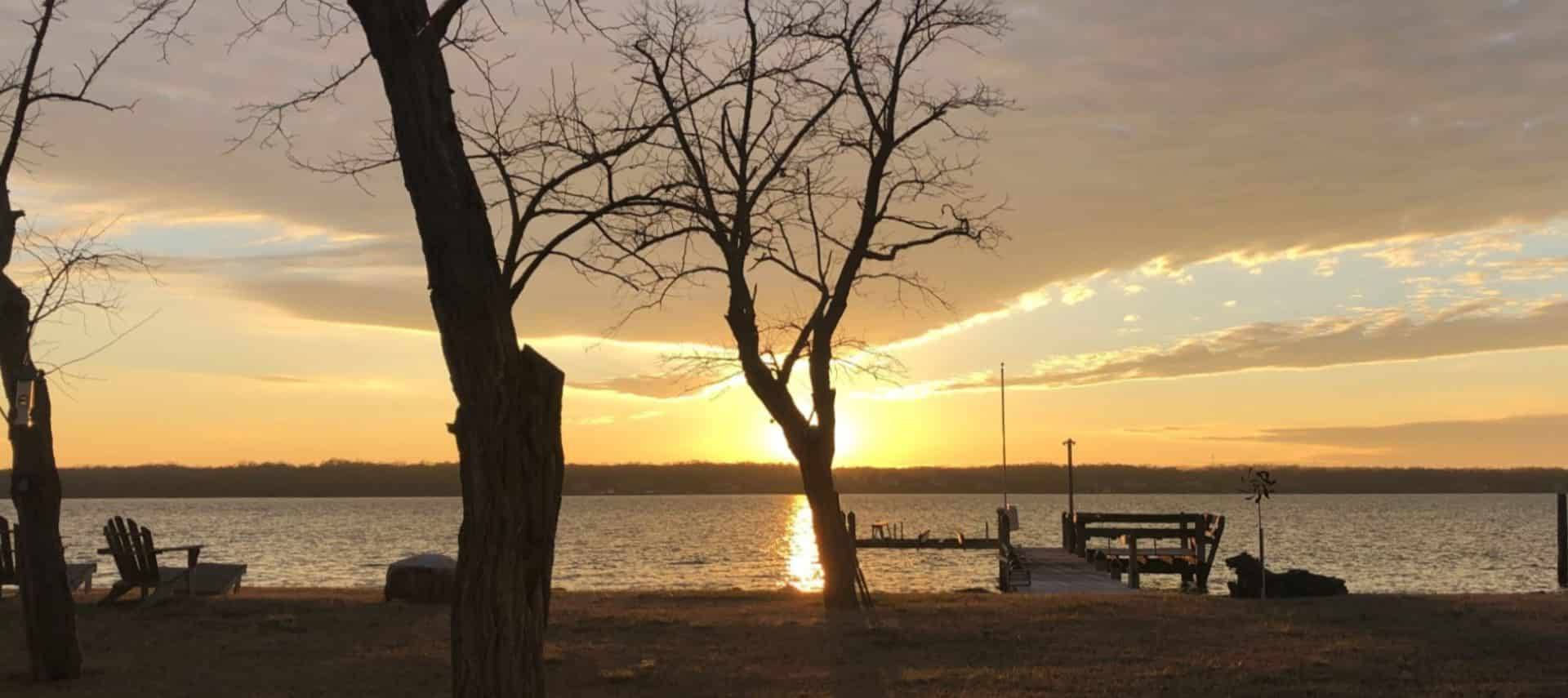 View of a small pier looking out to the water with land in the background and the setting sun
