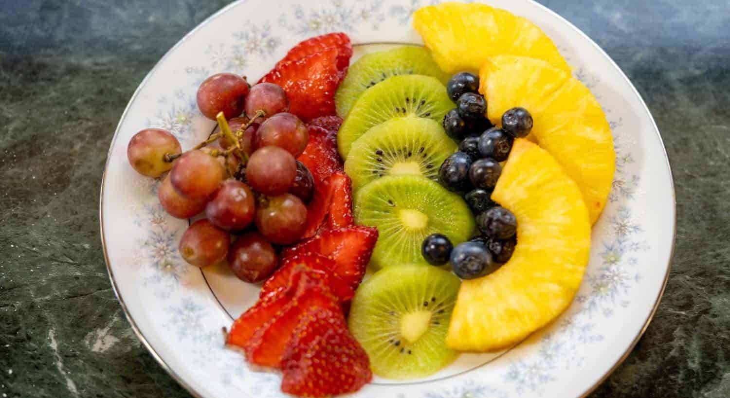 Close up view of sliced strawberries, kiwi, and pineapple, grapes and blueberries